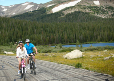 Couple riding optibikes with snowy mountains and lake in the background