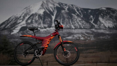 A custom red and orange flame painted Optibike R15 sits in front of snowy mountain peaks