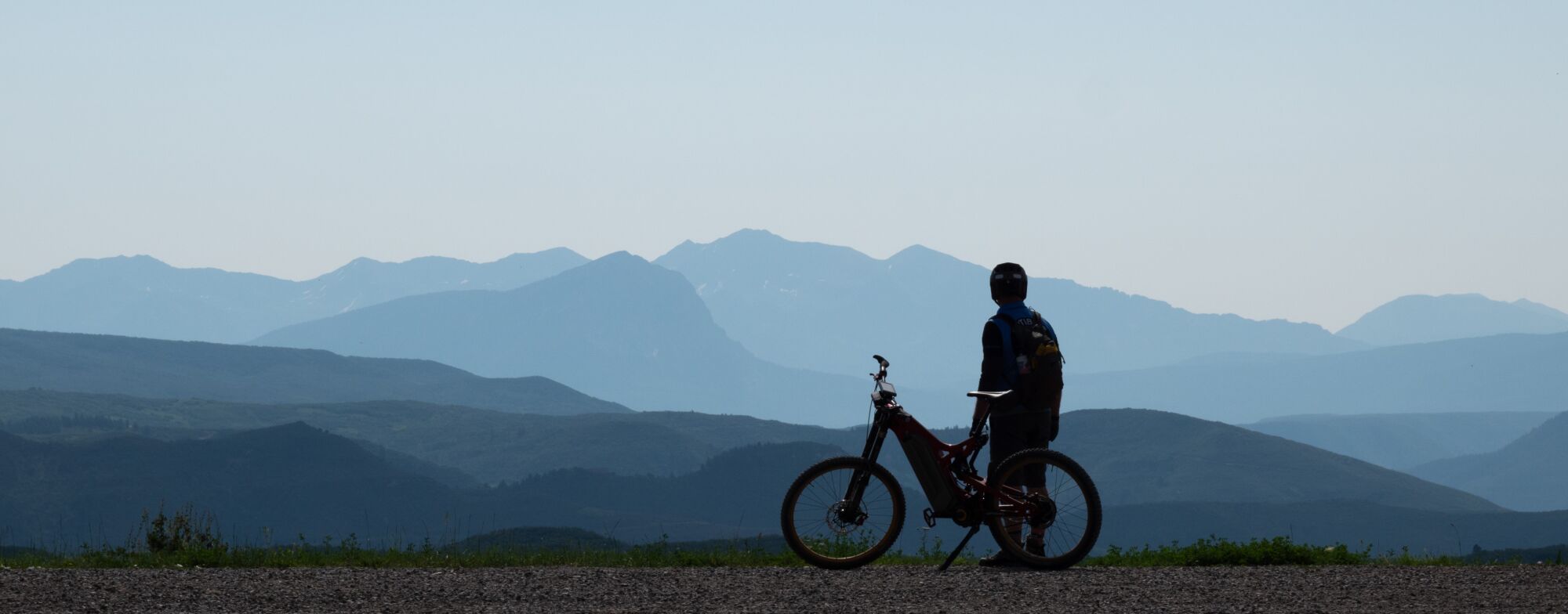 A silhouette of an Optibike R22 Everest with the rider looking out over jagged mountains in the distance.