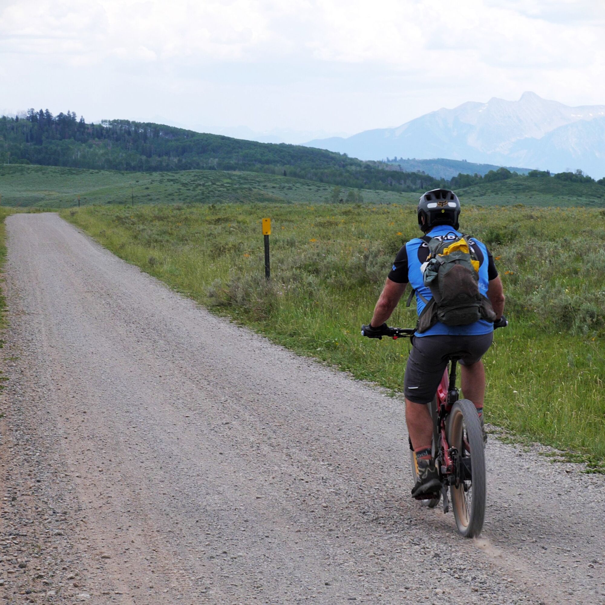 An Optibike R22 Everest rides down a gravel road, you can see snow capped mountains off in the distance